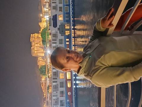 Woman posing on a boat with a historical site in the background.