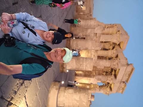 Two people posing in front of ancient temples at dusk with other people in the background.