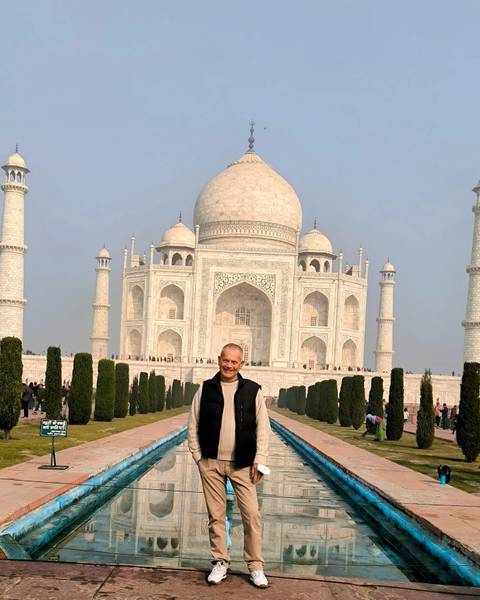 Person standing in front of the Taj Mahal with gardens and a marble pathway.