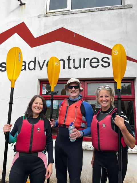 Group of people dressed for kayaking holding paddles in front of an adventure building.