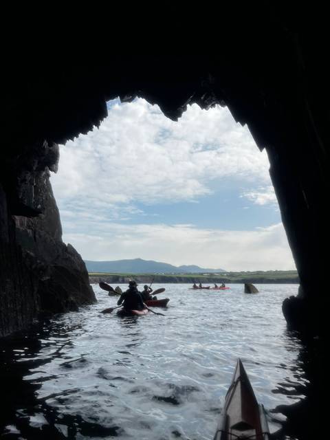 View from inside a cave with kayakers on the water outside.