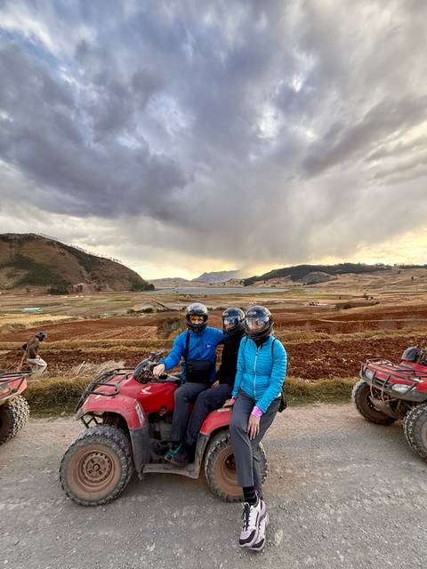 Three people in helmets riding ATVs in a rural landscape.