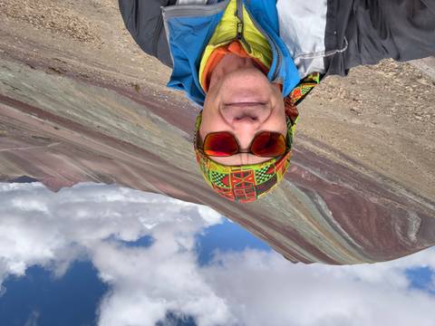 Man in colorful attire posing in front of Rainbow Mountain.