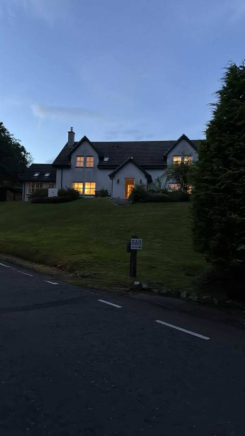       A house with illuminated windows at dusk, with a B&amp;B sign.
  