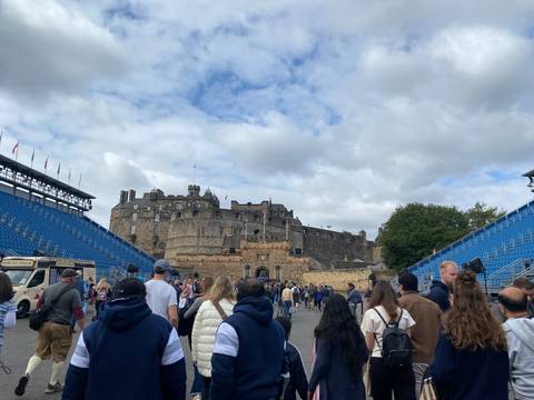 A crowd of people walking towards a large stone fortress with blue temporary seating.