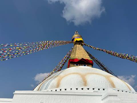       Baudhanath Stupa with prayer flags against a blue sky.
  