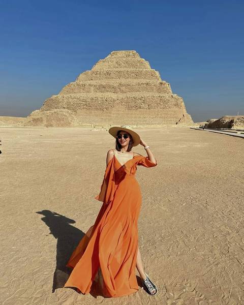       Woman in a dress standing in front of a pyramid in the desert.
  