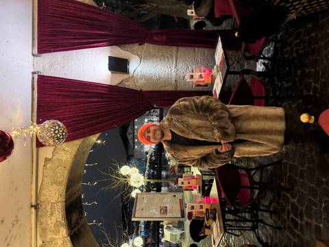 Person in a fur coat standing under a stone arch with festive decorations.
