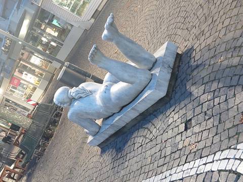 Stone statue of a reclining figure in a town square.