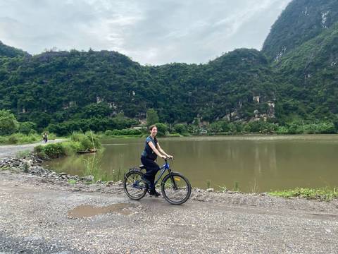       Woman cycling on a dirt road by a lake with hills in the background.
  