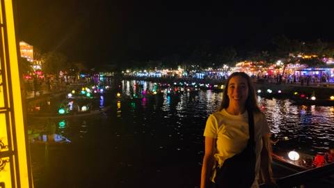 Woman standing by a river with lanterns at night.