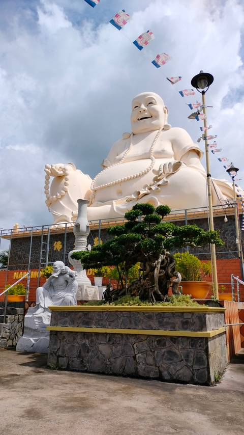       Large statue of a laughing Buddha with bonsai tree.
  