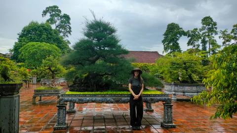       Woman in a garden with bonsai trees and a red brick path.
  