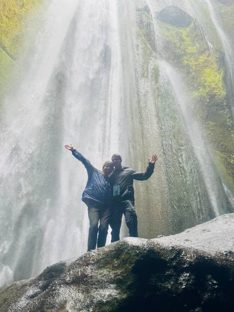 Two people posing under a waterfall.