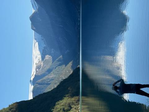 Man taking a photo of a lake with mountains in the background.