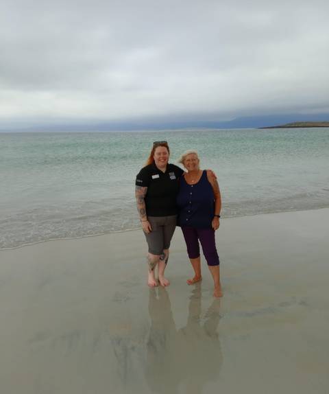 Two people standing on a sandy beach with the sea in the background.