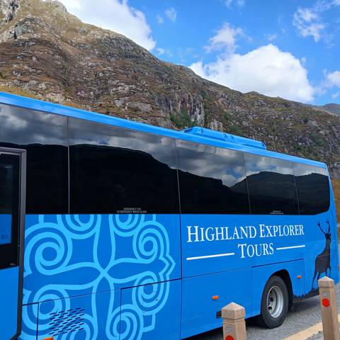 Tour bus with Highland Explorer Tours branding against a mountainous backdrop.