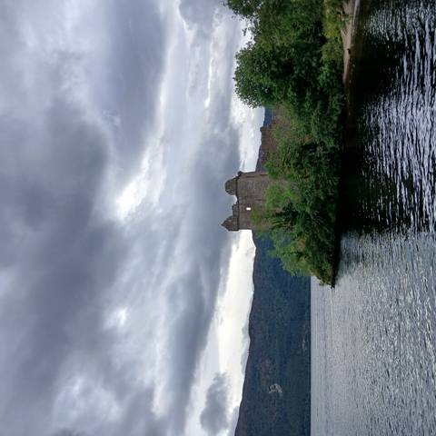 Old castle ruins by a lake under a cloudy sky.