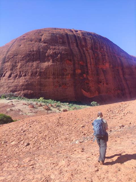       Person hiking near a massive red rock wall.
  