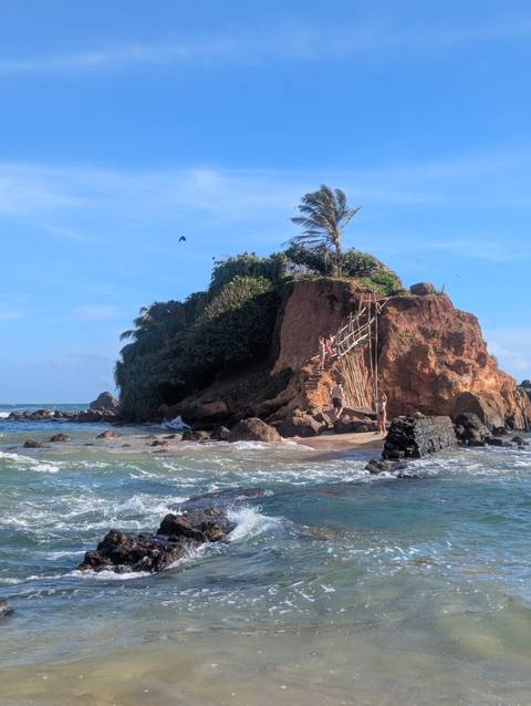 Beach with rocky cliffs and people around.