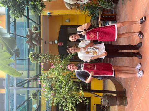 Three people in aprons posing in a courtyard.