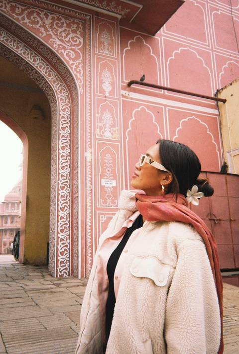       A woman standing in front of a pink wall with ornamental designs.
  