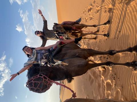 Two people riding camels in a desert landscape.