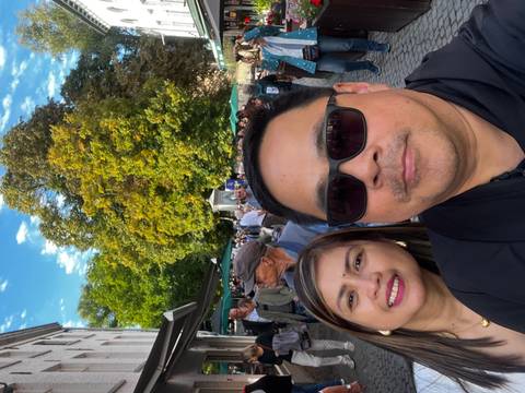       A couple taking a selfie in a park with people in the background.
  