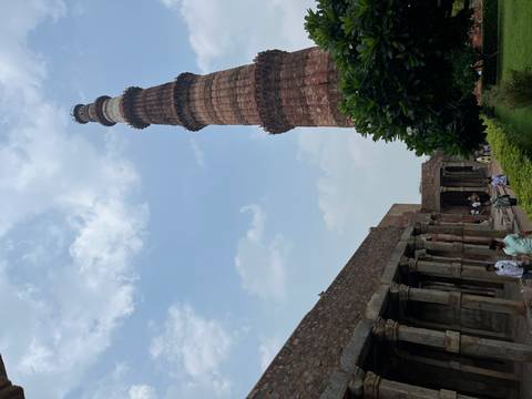       People walking near an ancient stone structure and tall minaret.
  