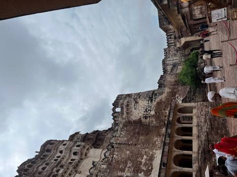       People walking by an ancient fort with high walls.
  