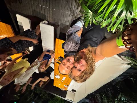 Group of people gathered around a casual outdoor area, with some taking a selfie.