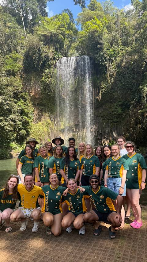 Group of people in Australian shirts posing in front of a waterfall.