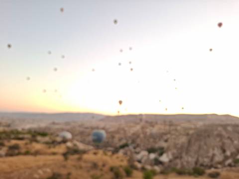 Blurry image of hot air balloons over a landscape at sunrise.