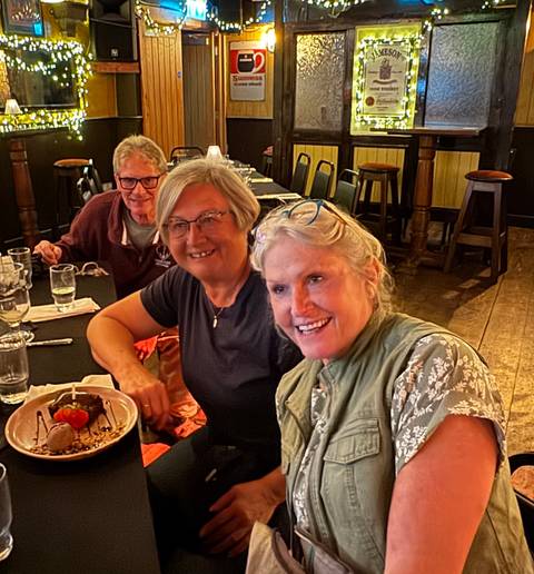 Three people smiling at a dining table with food in front of them.