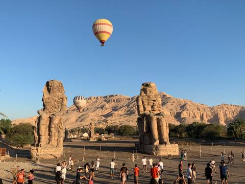 Two giant stone statues with hot air balloons overhead.