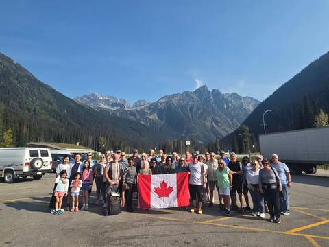 Group of people holding a Canadian flag in a mountainous region.