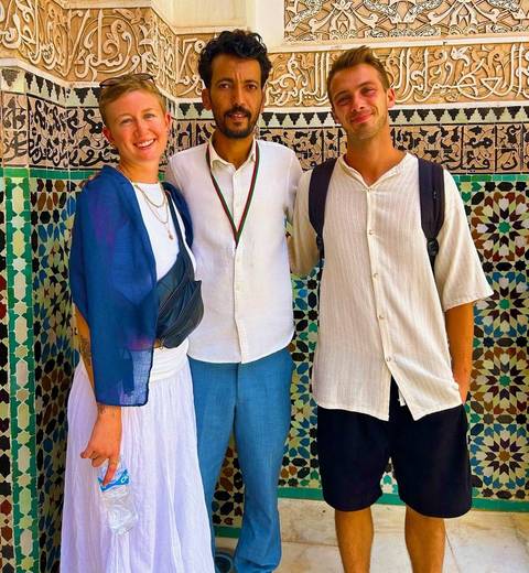       Three individuals standing in front of a colorful mosaic-tiled wall.
  