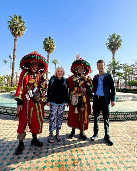       Tourists posing with local performers in traditional attire by a fountain.
  