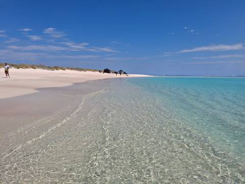 Sandy beach with clear blue waters and people walking.