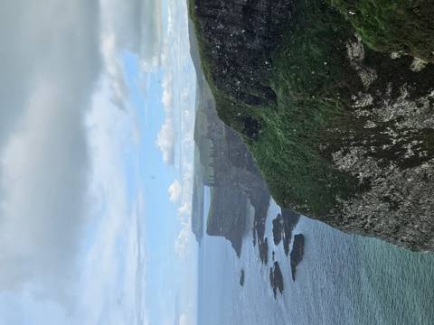Dramatic coastline with cliffs and ocean under a cloudy sky.