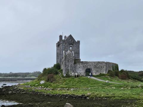 Old stone castle on a grassy hill with surrounding walls.