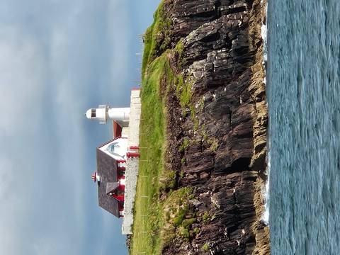 Lighthouse and building on a cliff edge overlooking the sea.