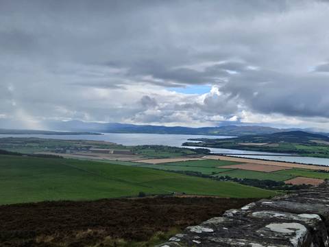 Expansive view of patchwork fields and water under a cloudy sky.