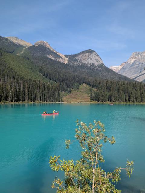 Canoe on a turquoise lake with forest and mountains in the background.