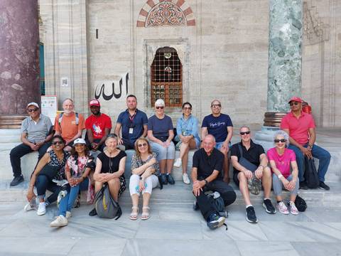       Tourists seated on stairs in front of a grand mosque entrance.
  