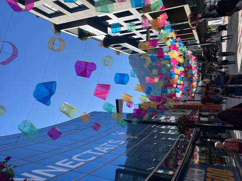       City street with colorful hanging lanterns and people walking.
  