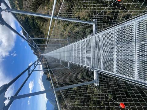       Metal suspension bridge over a mountainous landscape.
  