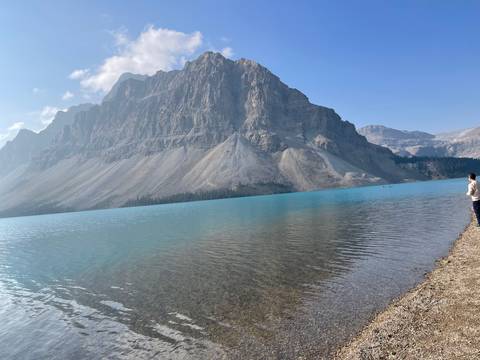 Person standing by a vast turquoise lake with mountain view.