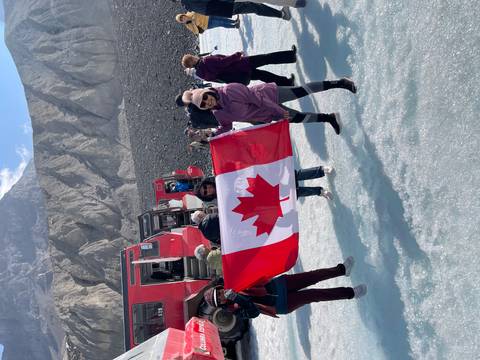 Group holding a Canadian flag on a snowy mountain with tour van.