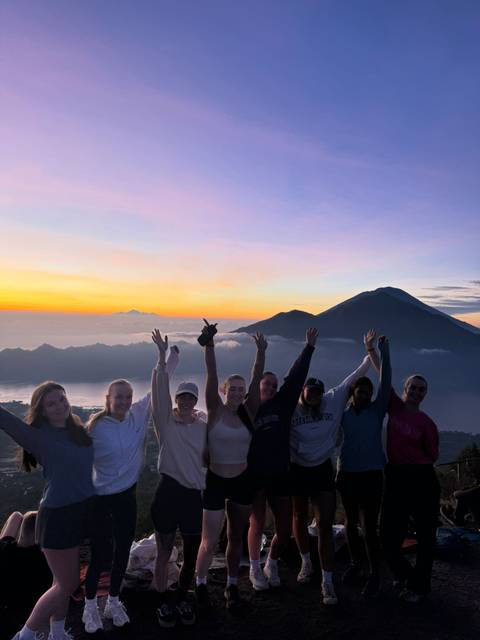 Group of people cheering at sunrise on a mountaintop.